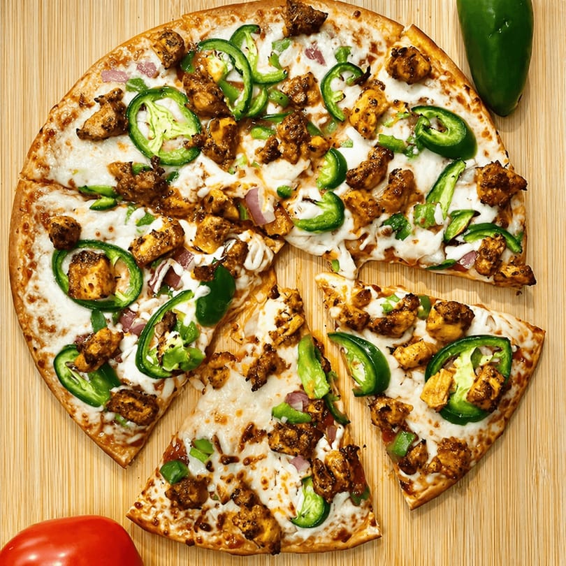 Chicken tikka pizza with jalapenos, onions, and melted cheese on a wooden board.