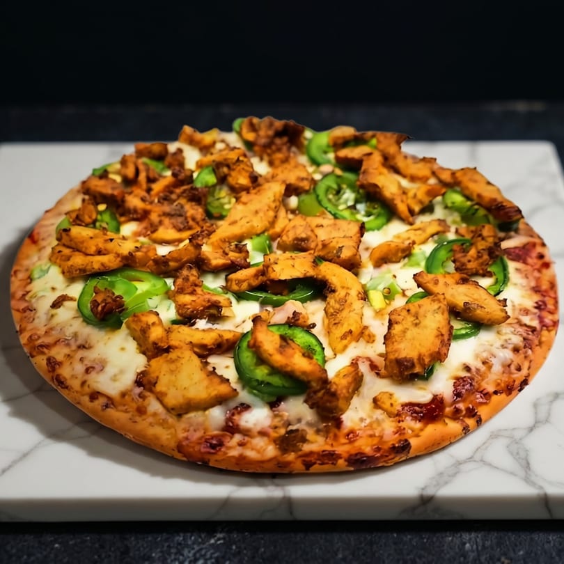 A whole chicken and jalapeño pizza with melted cheese on a white marble board.