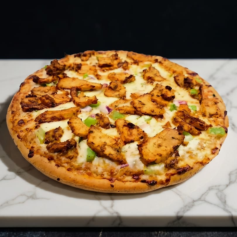 A whole chicken pizza with melted cheese, green peppers, and red onions on a marble surface.