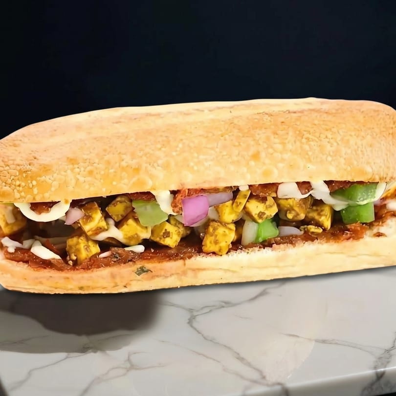 A close-up of a submarine sandwich filled with paneer, onions, and green peppers.